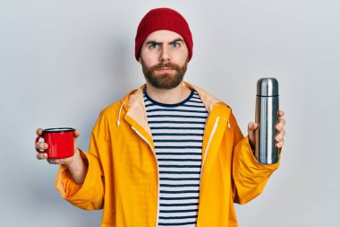 Kafkas sakallı, elinde bir fincan kahve, termo şüpheci ve gergin bir adam sorun yüzünden surat asıyor. negatif kişi. 