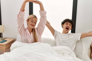 Genç ve güzel bir çift kollarını esnetiyor ve yatakta oturuyorlar..