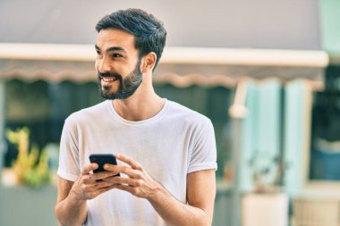 Genç İspanyol adam şehirde akıllı telefon kullanarak mutlu gülümsüyor..
