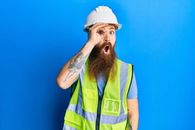 Uzun sakallı, güvenlik kaskı takan ve yansıtıcı ceket giyen kızıl saçlı adam şaşırmış yüz ifadesiyle şaşırmış, parmaklarından bakan gözler. İnançsız ifade. 