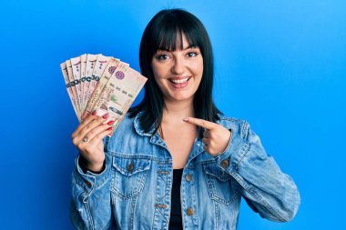 Suudi Arabistan 'ın riyal banknotlarını tutan genç İspanyol kadın mutlu bir şekilde el ve parmağıyla işaret ediyor. 