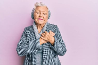 Kış süveteri giyen, elleri göğsünde gülümseyen, yüzünde minnet ifadesi olan yaşlı gri saçlı kadın. sağlık kavramı. 