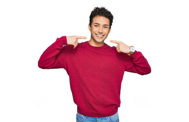 Gündelik kıyafetler giyen, neşeli gülümseyen, parmaklarıyla ve ağzıyla işaret eden genç yakışıklı bir adam. diş sağlığı kavramı. 