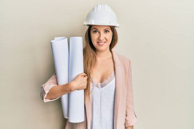 Güvenlik kaskı takan genç sarışın kadın elinde planlar tutuyordu. Pozitif ve mutlu görünüyordu. Kendine güvenen bir gülümsemeyle dişlerini gösteriyordu. 