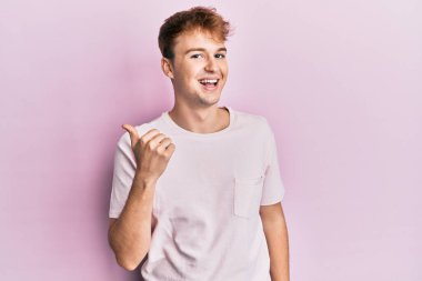 Gündelik tişörtler giyen genç beyaz bir adam baş parmağını yukarı kaldırıyor ve ağzı açık gülümsüyor. 