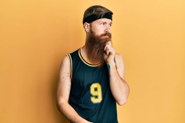 Uzun sakallı, basketbol forması giyen, elleri çenesinde soru soran, düşünceli bir adam. Düşünceli bir yüzle gülümsüyor. şüphe kavramı. 