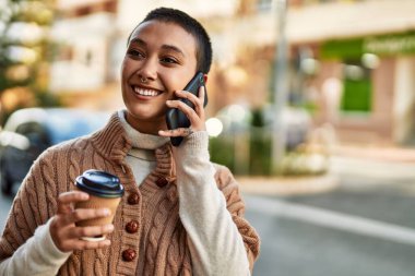 Kısa saçlı, gülümseyen, mutlu, kahve içen ve telefonda konuşan İspanyol bir kadın.