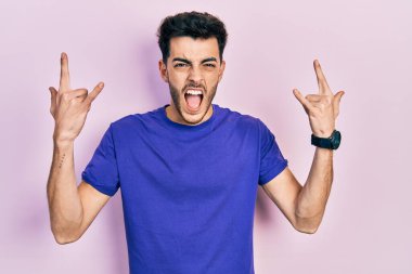 Günlük tişört giyen genç İspanyol adam çılgın bir ifadeyle bağırıyor elleri havada rock sembolü yapıyor. Müzik yıldızı. ağır müzik konsepti. 