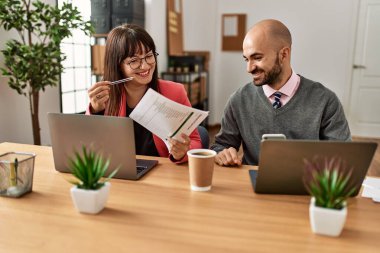 Ofiste bilgisayar ve akıllı telefon kullanarak çalışırken gülümseyen iki İspanyol iş adamı..