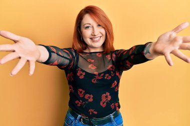 Güzel kızıl saçlı kadın sıradan kıyafetler giyip kameraya bakıyor. Sarılmak için kollarını açmış gülümsüyor. Mutluluğu kucaklayan neşeli bir ifade.. 