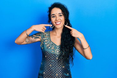 Bindi ve geleneksel kurta elbisesi giyen neşeli bir şekilde gülümseyen ve parmaklarıyla ve ağzıyla işaret eden genç bir kadın. diş sağlığı kavramı. 