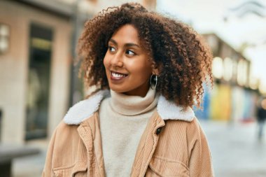 Genç Afrikalı Amerikalı kadın gülümseyerek şehirde mutlu mesut duruyor..