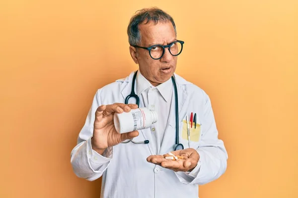 中年インド人男性を身に着けている医師の制服ショック顔に処方薬を保持 懐疑的で皮肉を探して オープン口で驚いて — ストック写真