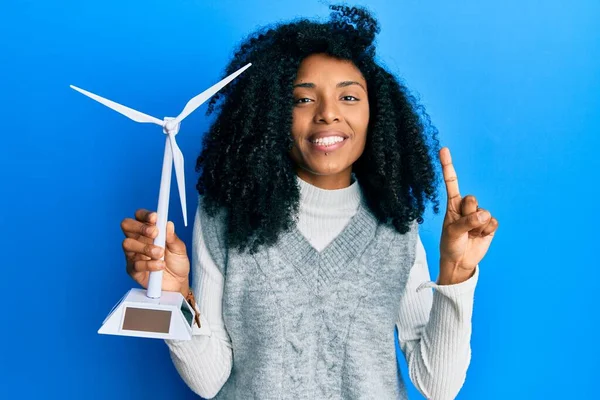 アフリカ系アメリカ人の女性アフロヘアは 幸せな顔をしたアイデアや質問を指差す指で笑顔再生可能エネルギーのためのソーラー風車を保持し ナンバーワン — ストック写真