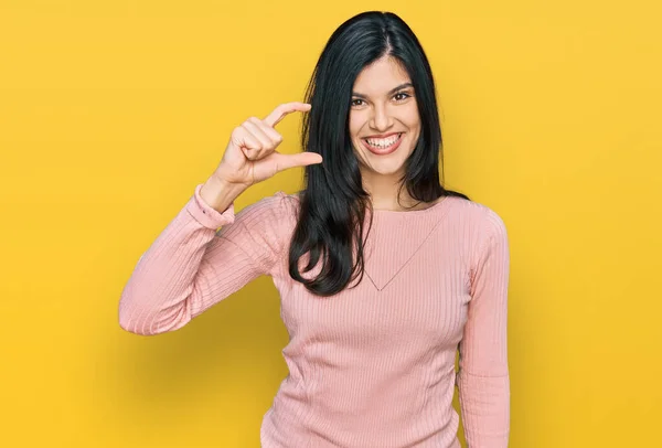 カジュアルな服を着た若いヒスパニック系の女性が笑顔で 指を見てカメラで小さなサイズの看板を行う手で自信を持ってジェスチャー 概念を測定し — ストック写真