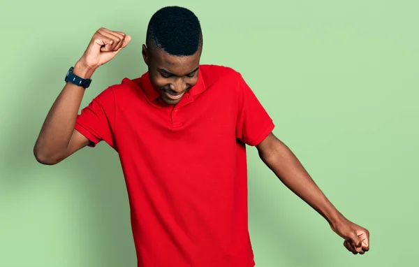 身穿休闲红T恤的年轻的非洲裔美国人快乐而快乐地跳舞 微笑着随意而自信地听着音乐 — 图库照片