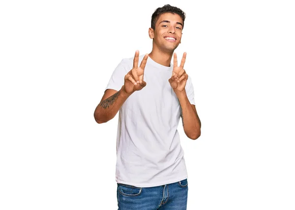 年轻英俊的非洲裔美国男人穿着休闲的白色T恤 微笑着看着摄像机 手指头在做胜利的标志 第二点 — 图库照片