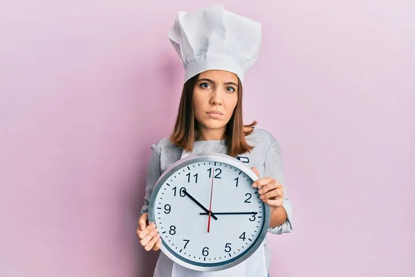 プロの料理人の制服を着た若い美少女と 真剣な表情でリラックスした時計を手にした帽子 カメラを見ているだけで — ストック写真