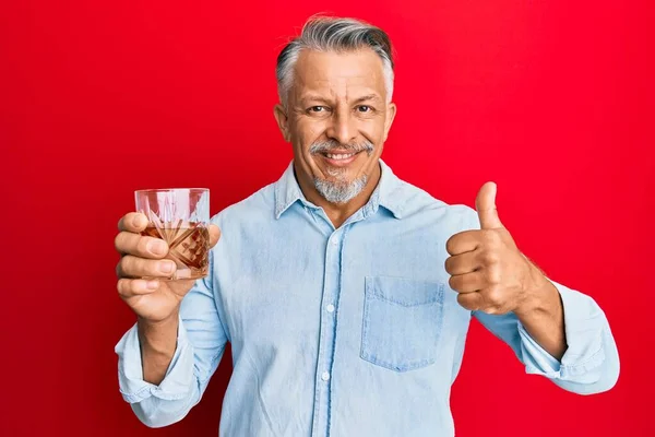 中年白髪の男飲むガラスのウイスキー笑顔幸せと正 親指アップ行う優れた承認サイン — ストック写真