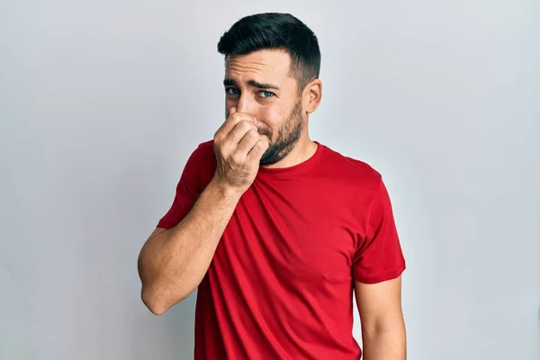 若いヒスパニック系の男性は 鼻の上に指で息を保持し 何か臭いと嫌な 耐え難い匂いを嗅ぐカジュアルな服を着て 臭いが悪い — ストック写真