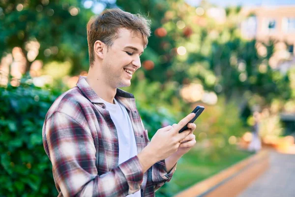 Νεαρός Καυκάσιος Άνδρας Χαμογελά Χαρούμενος Χρησιμοποιώντας Smartphone Στο Πάρκο — Φωτογραφία Αρχείου