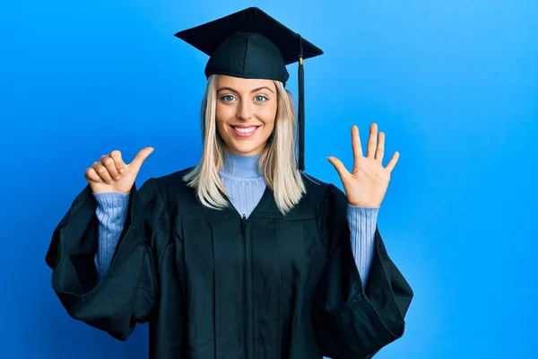 Schöne Blonde Frau Trägt Abschlussmütze Und Zeremoniengewand Und Zeigt Mit — Stockfoto