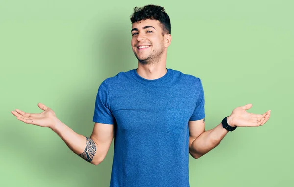 両手を開いて手のひらを示す笑みを浮かべてカジュアルなTシャツを着て若いヒスパニック系の男 プレゼンテーションと広告の比較とバランス — ストック写真