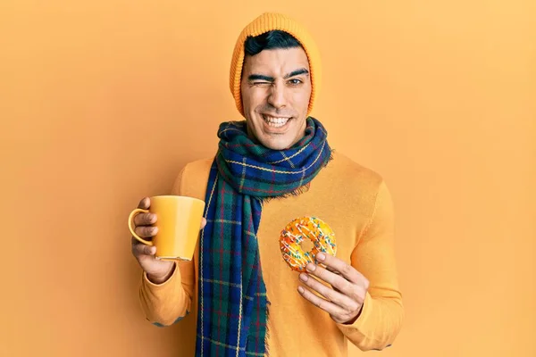 Hombre Hispano Guapo Comiendo Donut Bebiendo Café Guiño Mirando Cámara —  Fotos de Stock