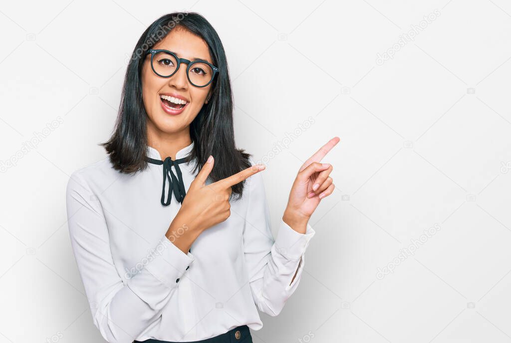 Beautiful asian young woman wearing business shirt and glasses smiling and looking at the camera pointing with two hands and fingers to the side. 