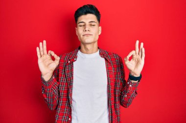 Günlük kıyafetler giyen genç İspanyol adam rahatla ve gözleri kapalı gülümse parmaklarıyla meditasyon hareketi yapıyor. yoga konsepti. 