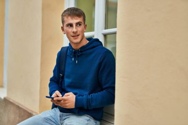 Üniversitede akıllı telefon kullanarak mutlu gülümseyen genç sarışın öğrenci..