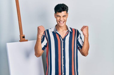 Boş tuvalin yanında dikilen genç İspanyol adam kollarını kaldırıp, gözlerini açarak başarının şaşkınlığını ve şaşkınlığını kutluyor. Kazanan konsept. 