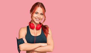 Spor kıyafetleri giyen, kulaklık takan, kollarını kavuşturup kameraya gülümseyen genç bir kadın. pozitif kişi. 