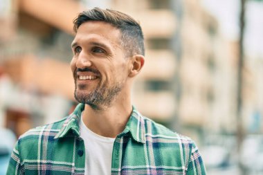 Genç beyaz adam gülümseyerek şehirde mutlu mesut duruyor..