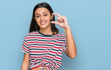 Gündelik kıyafetler giyen, gülümseyen, kendine güvenen, el hareketi yapan, parmaklarıyla işaret yapan ve kameraya bakan genç İspanyol kız. ölçüm kavramı. 