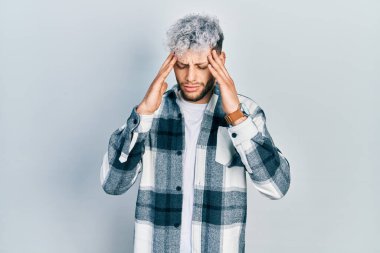 Modern boyalı saçı olan genç İspanyol bir adam stresten dolayı elleri başının üstünde olan günlük bir gömlek giyiyor. migren ağrısı. 