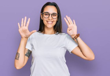 Gündelik beyaz tişört giyen genç İspanyol kadın dokuz numarayı gösterip işaret ederken kendine güvenen ve mutlu bir şekilde gülümsüyor.. 