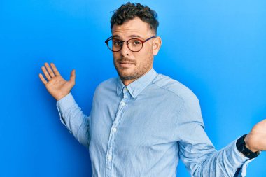 Sıradan kıyafetler giyen, gözlüklü, kafası karışık, elleri ve kolları havada bir İspanyol. şüphe kavramı. 