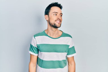 Gündelik kıyafetler giyen genç İspanyol bir adam yüzünde gülümsemeyle yan yana bakıyor, doğal bir ifade. Kendinden emin gülen. 