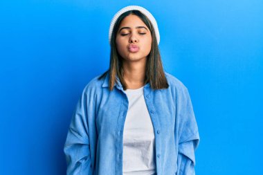 Şirin yün şapkalı genç Latin bir kadın kameraya bakıp havada öpüşürken güzel ve seksi görünüyor. aşk ifadesi. 