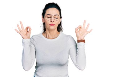 Gündelik kıyafetler giyen, gözleri kapalı gülümseyen genç İspanyol kadın parmaklarıyla meditasyon hareketi yapıyor. yoga konsepti. 