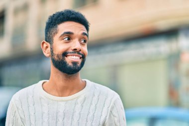 Genç Afrikalı Amerikalı adam gülümseyerek şehirde mutlu mesut duruyor..