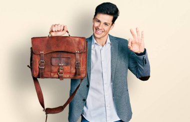 Genç İspanyol adam iş çantasını tutuyor. Parmaklarıyla imza atıyor, gülümsüyor. Mükemmel bir sembol. 