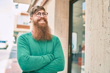 Kollarını kavuşturmuş genç İrlandalı adam gülümseyerek şehirde mutlu mesut yürüyor..