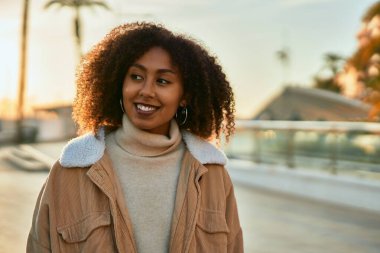 Genç Afrikalı Amerikalı kadın gülümseyerek şehirde mutlu mesut duruyor..