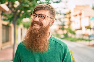 Kızıl sakallı genç İrlandalı adam şehirde mutlu bir şekilde yürürken gülümsüyor..