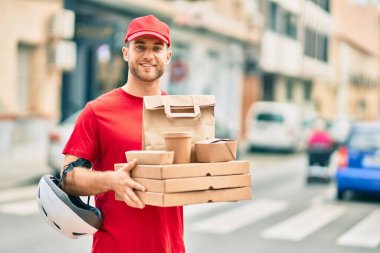 Beyaz tenli genç teslimatçı gülerek şehirde yemek dağıtıyor..