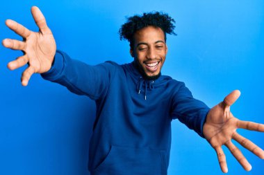 Sakallı, sıradan bir kazak giyen genç Afro-Amerikan adam kameraya bakıp sarılmak için gülümsüyor. Mutluluğu kucaklayan neşeli bir ifade.. 