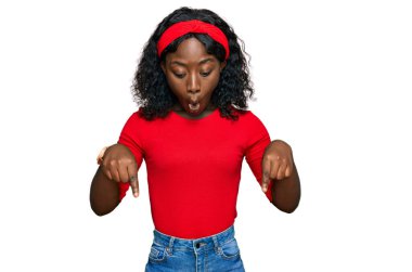 Güzel Afrikalı genç bir kadın günlük giysiler giyip parmaklarını göstererek reklamını yapıyor, şaşırmış yüzünü ve ağzını açıyor. 