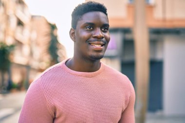Genç Afrikalı Amerikalı adam gülümseyerek şehirde mutlu mesut duruyor..